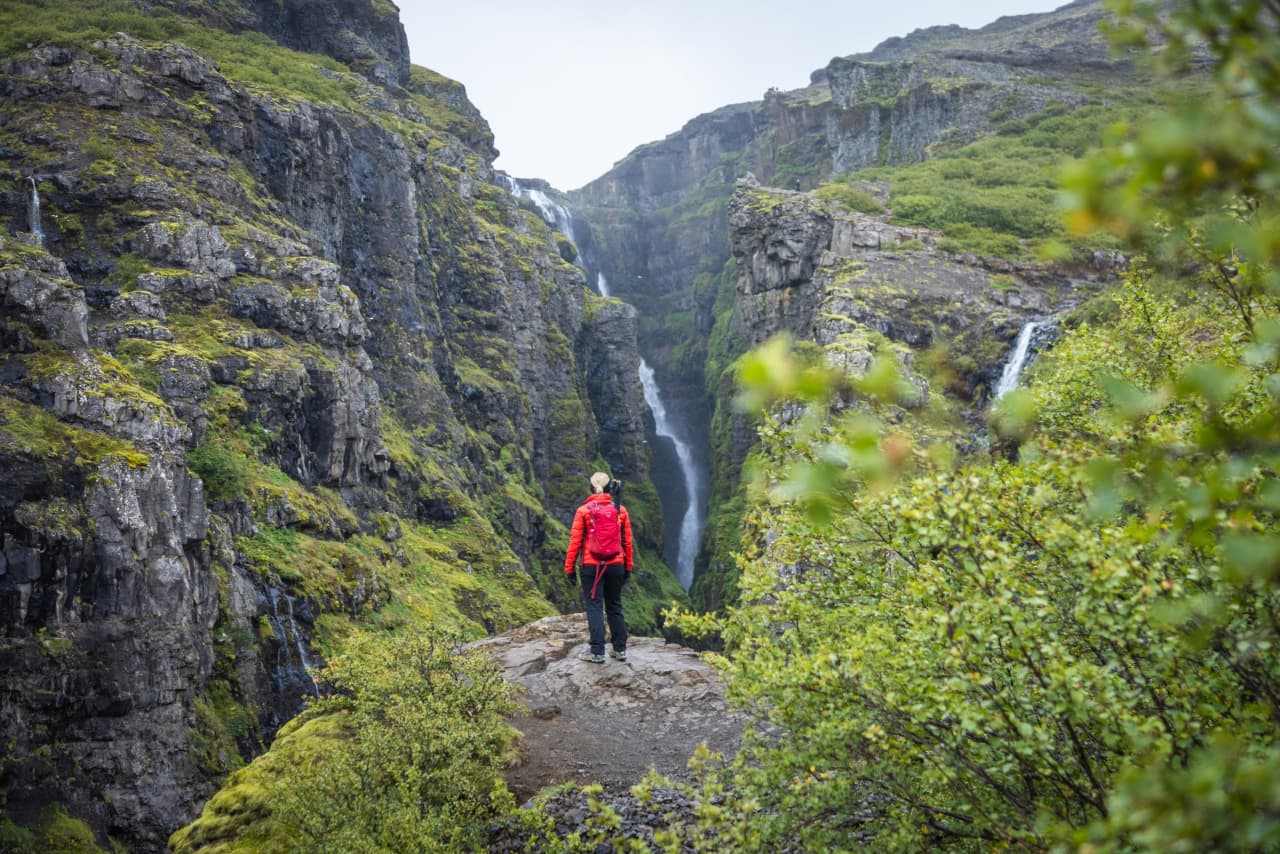 Hiker viewing Glymur waterfall in its canyon
